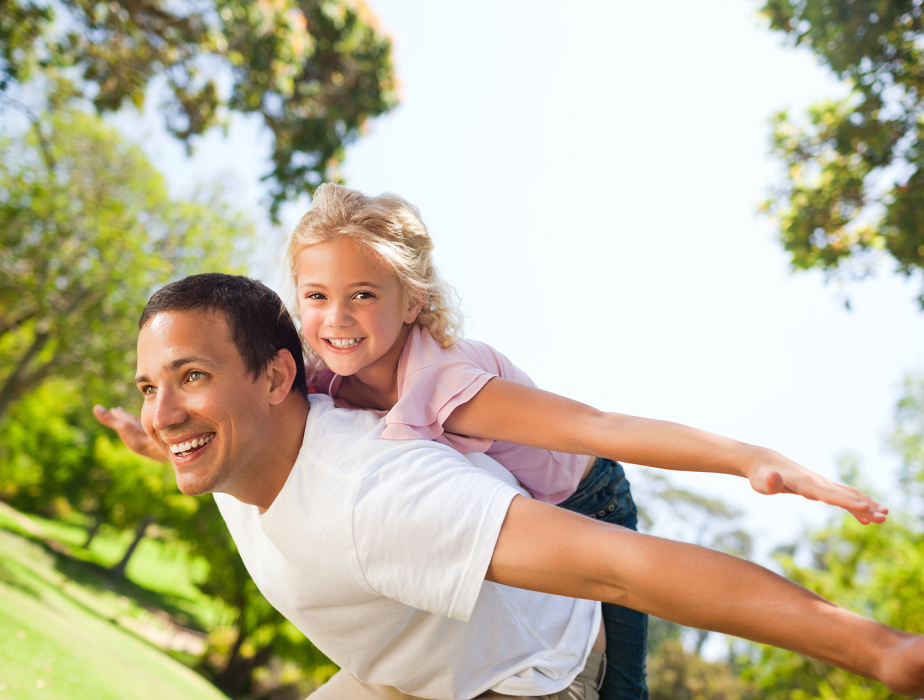 In this image, a father is playing with his daughter by lifting her on his back.