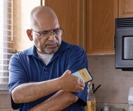 In this image, a man holds a mobile phone and checks his blood glucose.