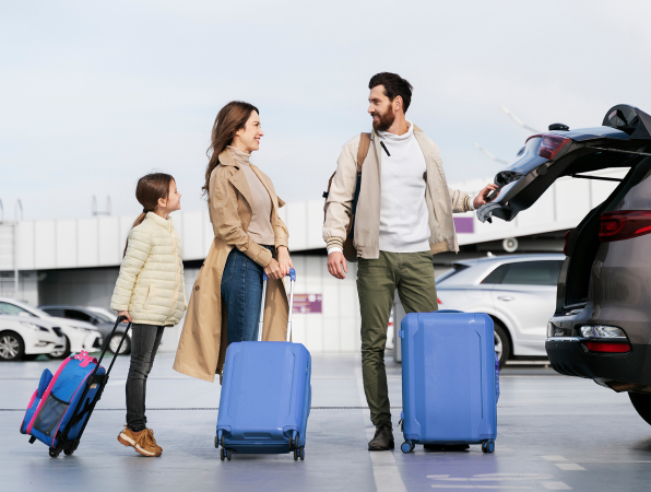 A picture of the family ready to go on the trip, standing by their car with luggage. 